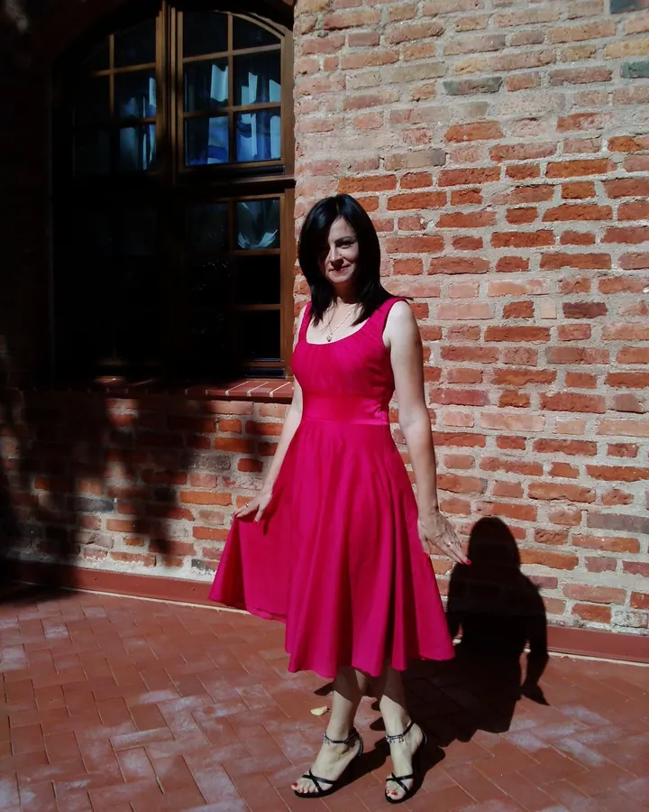Femme aux cheveux noirs en robe rouge, debout devant un mur en briques, regardant l'appareil photo