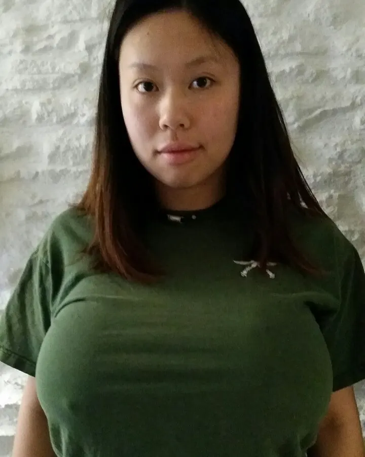 Femme aux cheveux noirs, en t-shirt vert, regardant l'appareil photo avec un visage neutre.