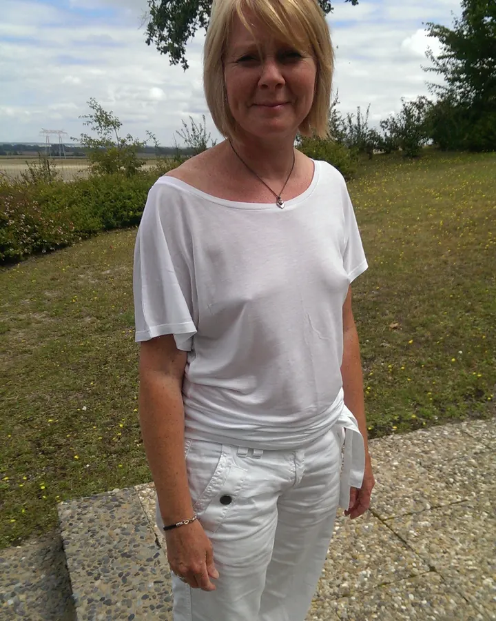 Femme aux cheveux blonds portant un bikini bleu et blanc, debout dans un cadre naturel.
