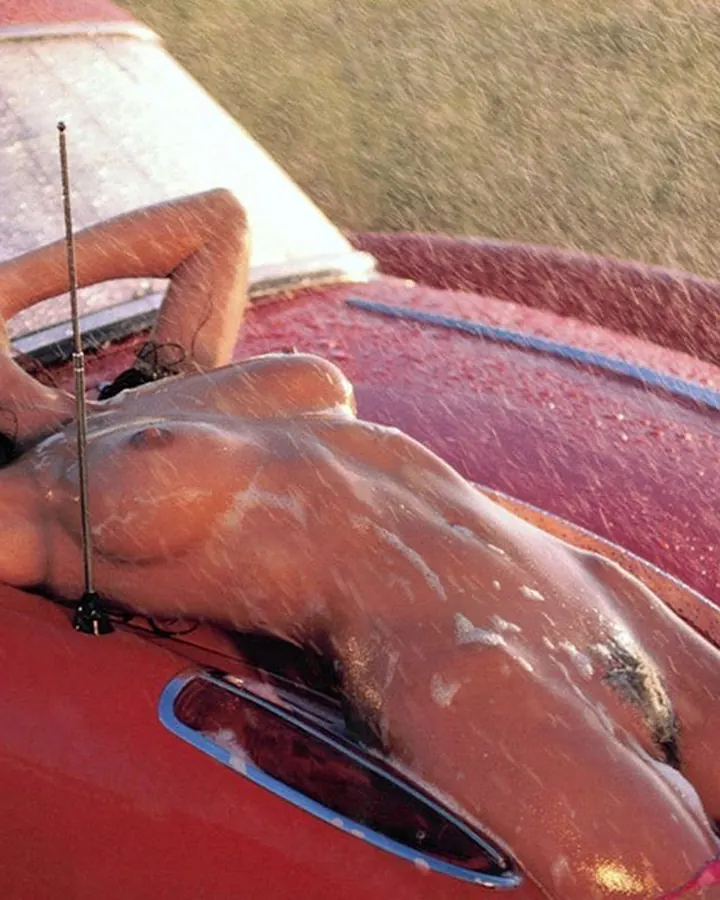 Femme aux cheveux bruns en maillot rose posant sur une voiture rouge