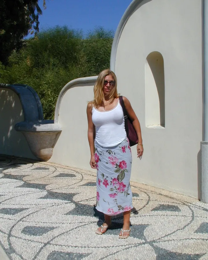 Femme blonde en haut blanc et jupe fleurie, posant en extérieur