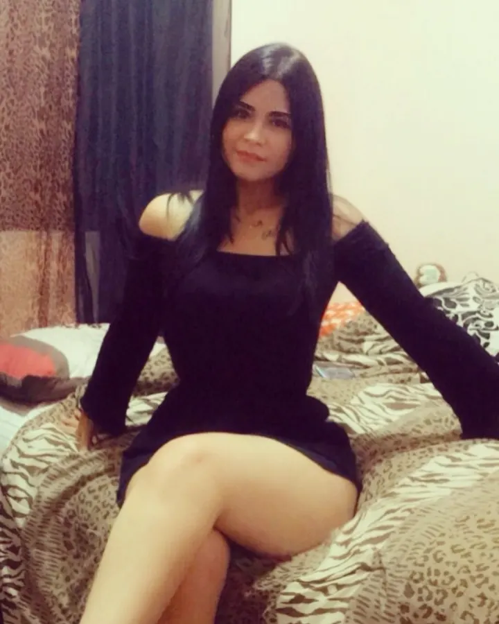 Femme aux cheveux noirs longs, en robe noire décolletée, assise sur un lit à motif zèbre