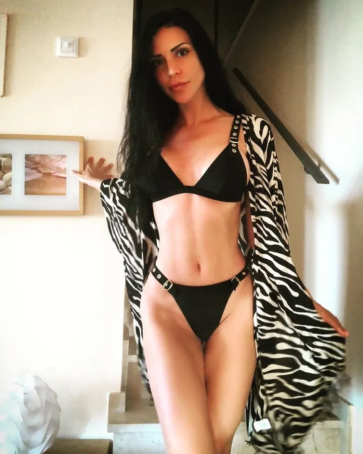 Femme aux cheveux bruns en robe noire, posant sur un canapé