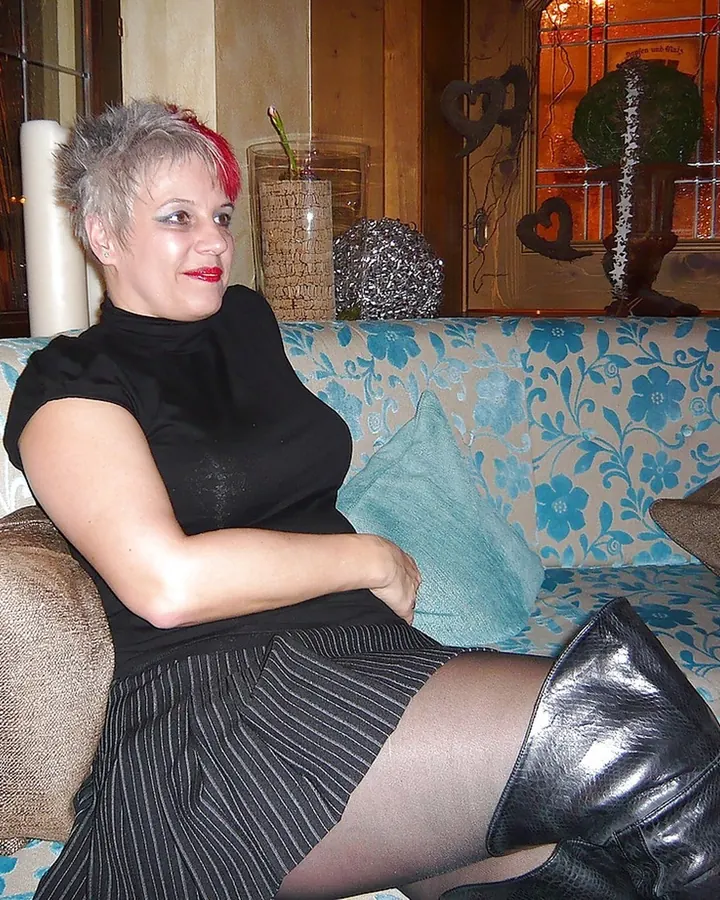Femme aux cheveux gris en robe noire, posant sur un canapé