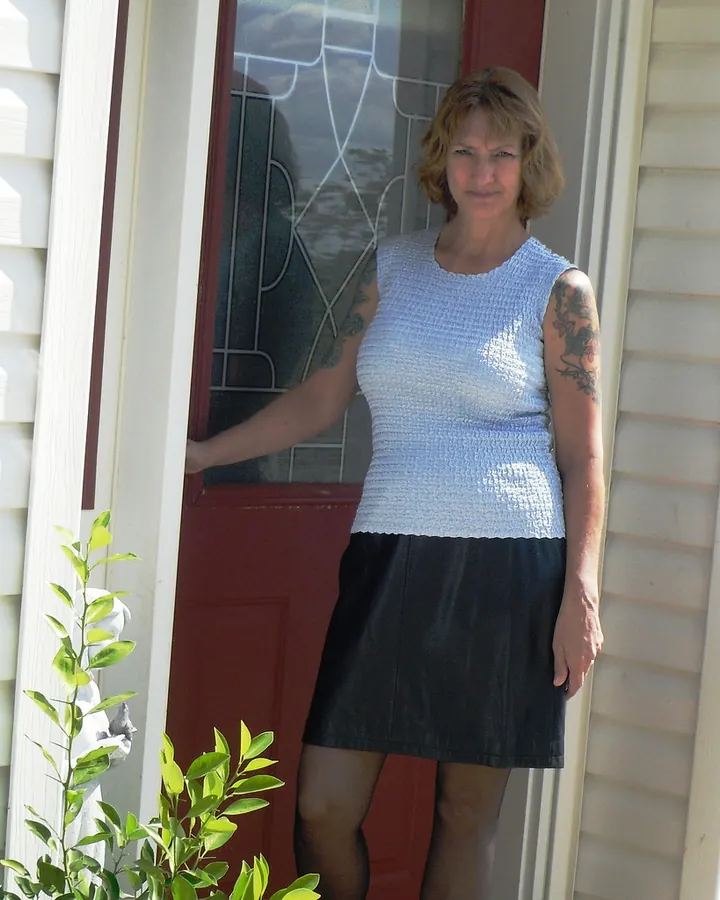 Femme aux cheveux blonds en robe bleue, posant sur un porche