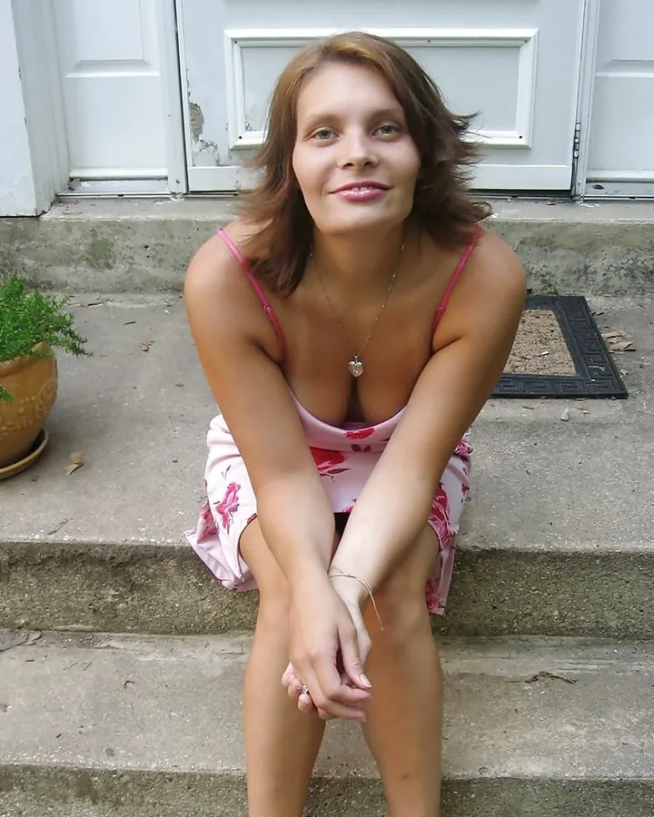 Femme aux cheveux châtains assise sur des marches extérieures, portant un maillot de bain rose à fleurs, les bras croisés sur les genoux, souriant doucement.