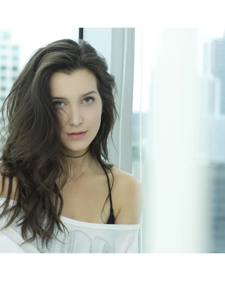Femme en débardeur blanc, regardant l'appareil photo, cheveux longs et ondulés.