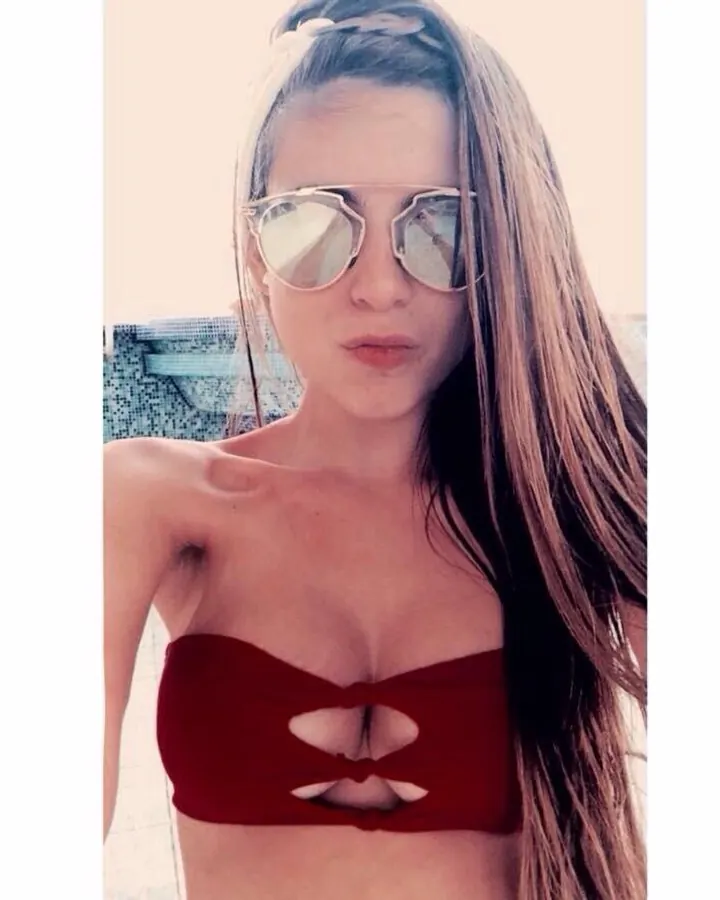Femme en haut rouge, lunettes de soleil, pose frontale, plage en arrière-plan