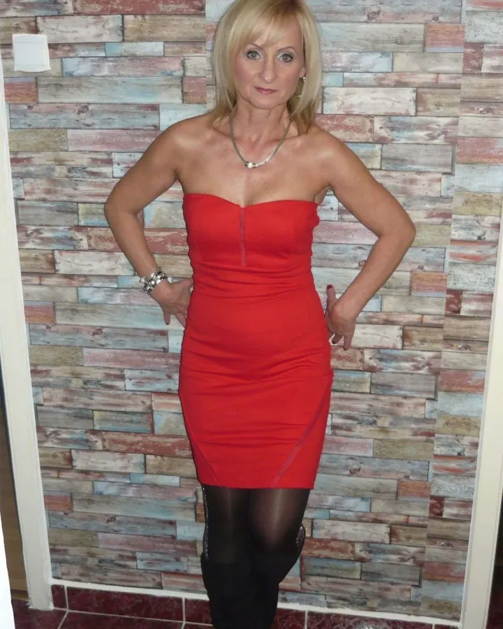 Femme blonde en robe rouge, pose frontale, mur en bois en arrière-plan