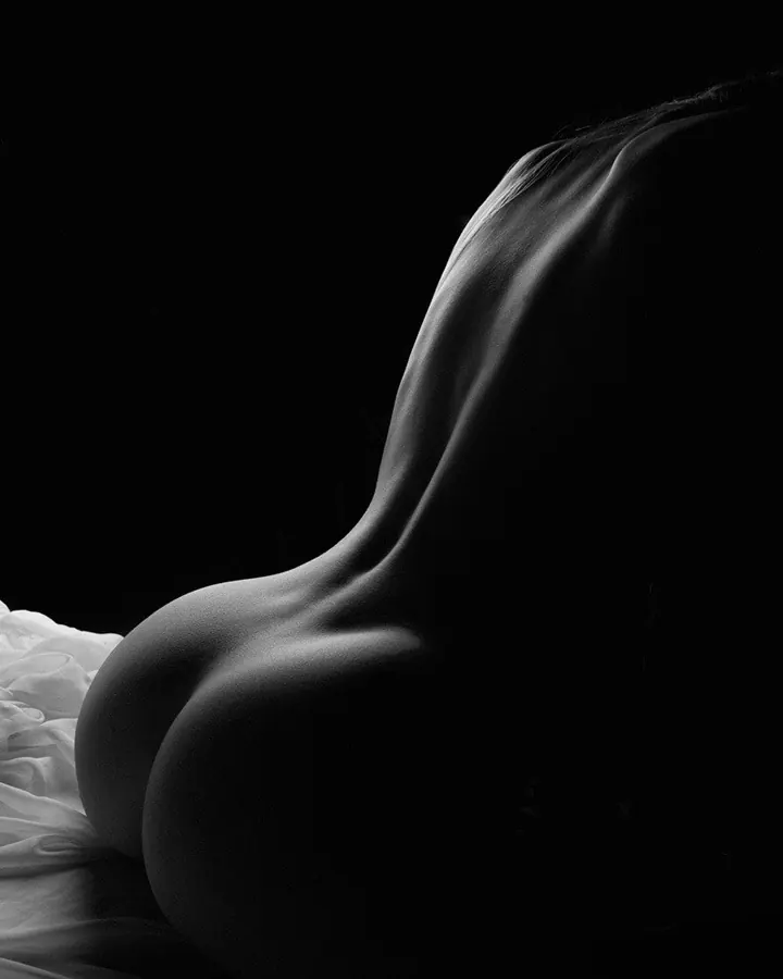 Photo en noir et blanc, silhouette féminine allongée, drapé blanc, lumière dramatique