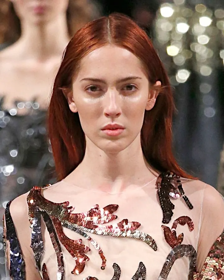 Femme aux cheveux bruns, en haut noir, prenant un selfie dans un miroir rond, dans une chambre moderne.