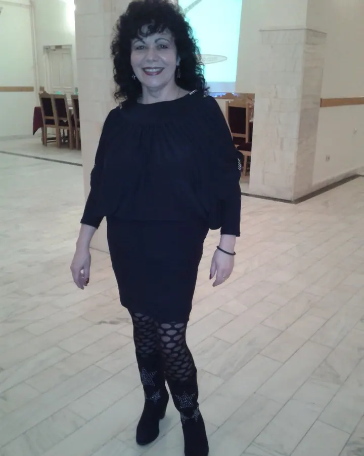 Femme aux cheveux bruns longs, portant un haut noir, assise sur un canapé noir, tenant un oreiller blanc, pieds nus.