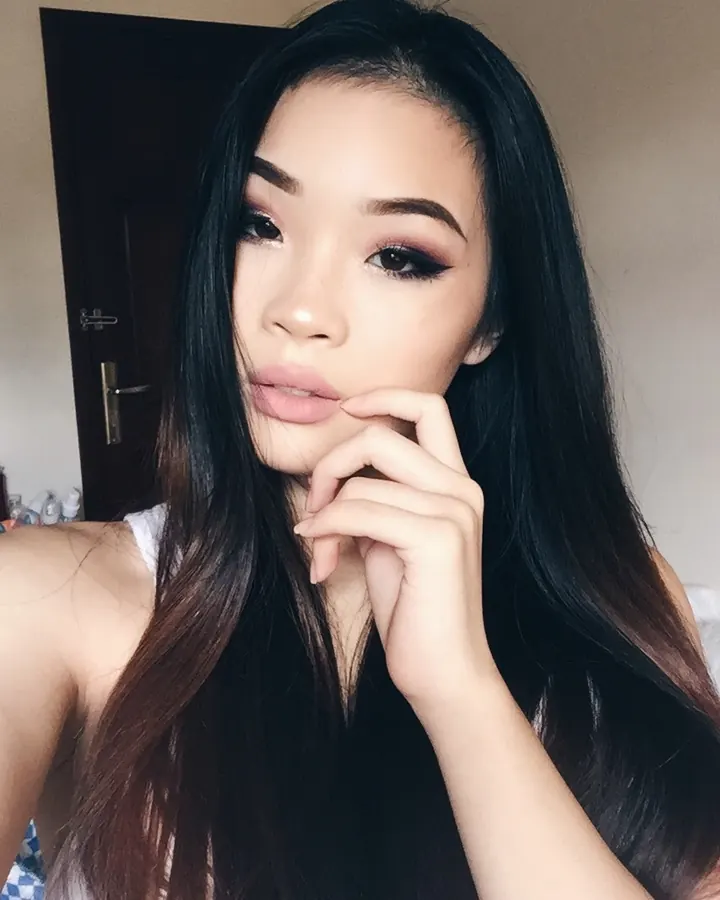 Jeune femme aux cheveux noirs, portant un haut blanc et un short rouge, debout dans une chambre.