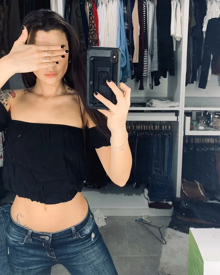 Femme aux cheveux châtains portant une robe noire en dentelle, assise sur un lit